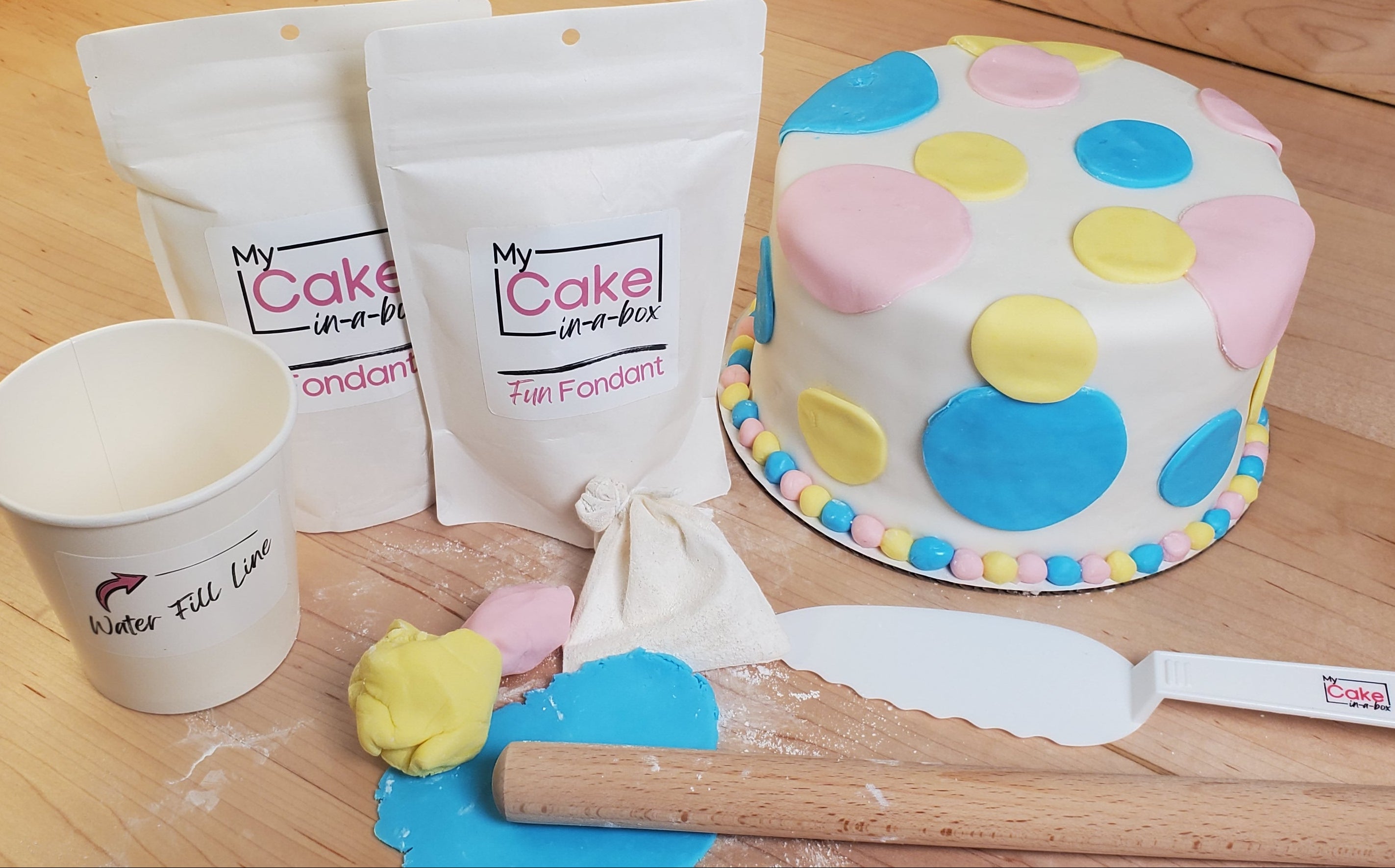 Cake decorating kit with polka dot cake, bags of frosting, tools on a wooden surface.